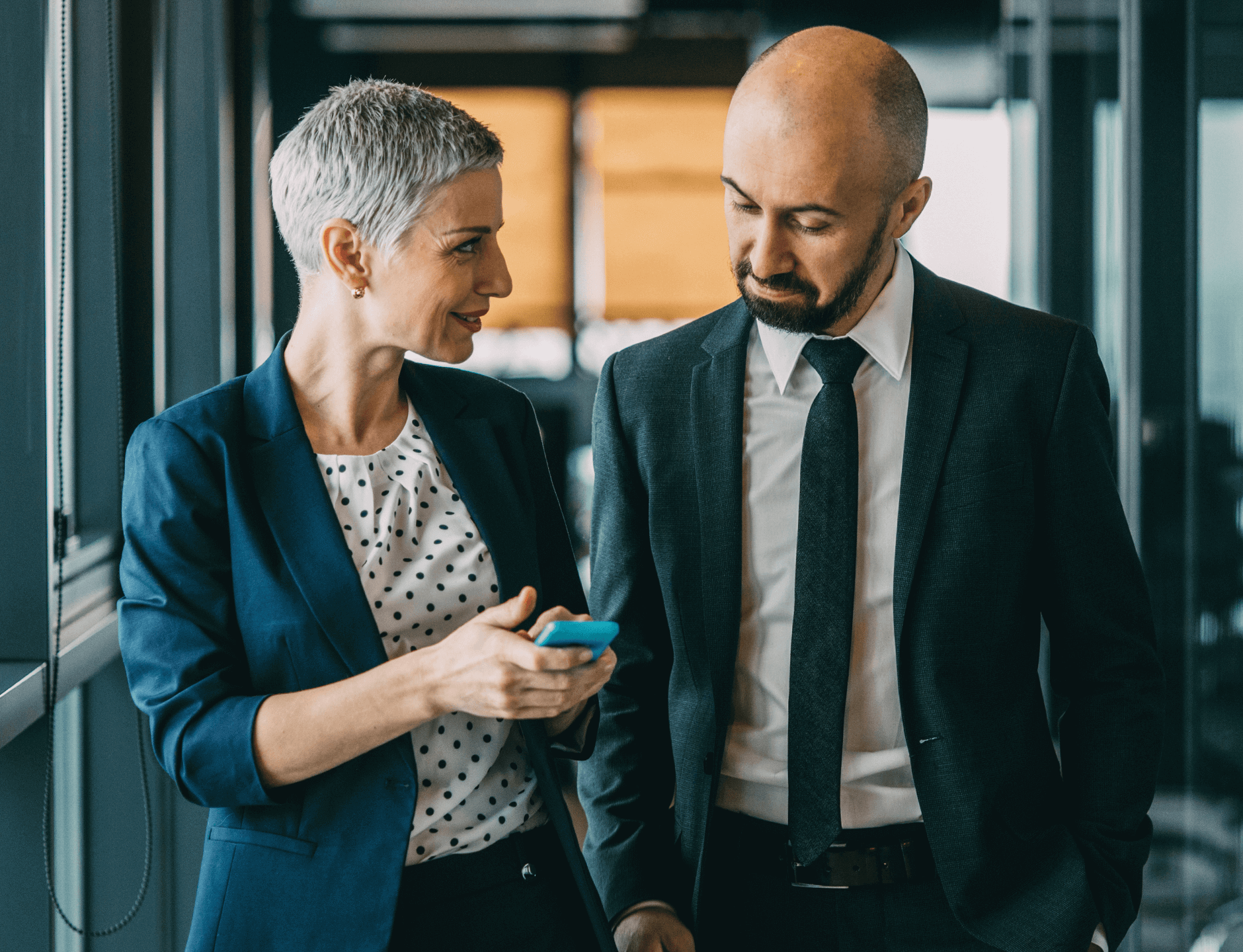 mature man and woman in office setting talking with one looking at mobile phone