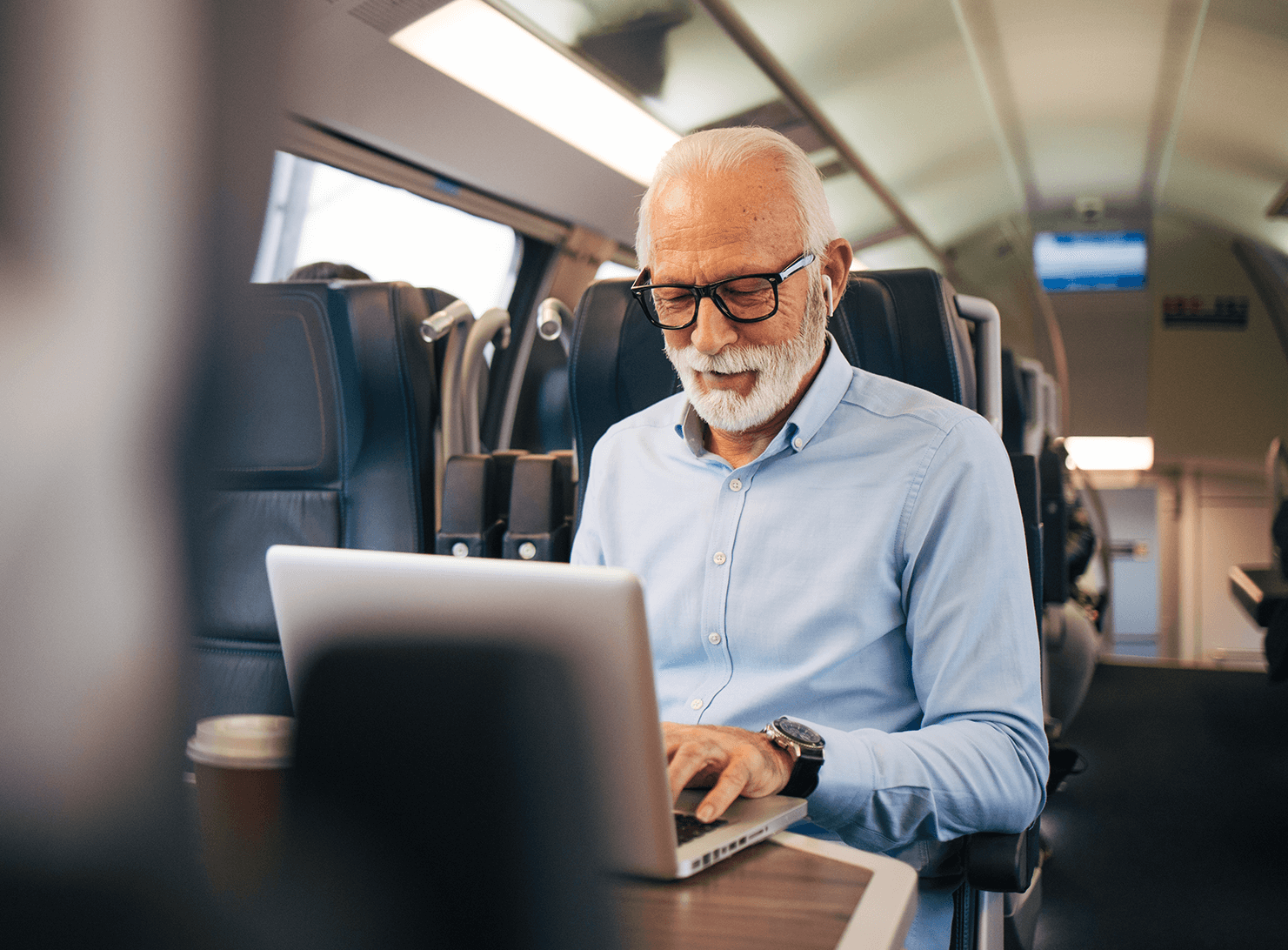 older business man riding on train seated at business table working on laptop