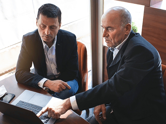 older business men discussing info on laptop screen