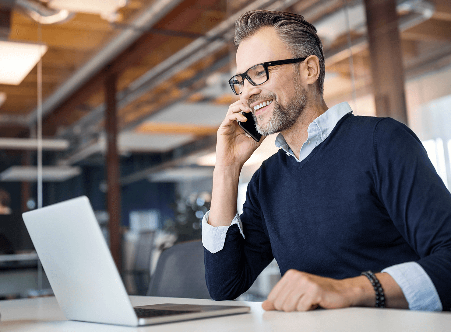 middleaged business man in sweater talking on cell phone while looking at laptop