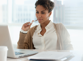 young African American business woman sitting, pen to face, in front of laptop image