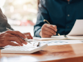 arm and hand view of business people sitting at table with papers and calculator