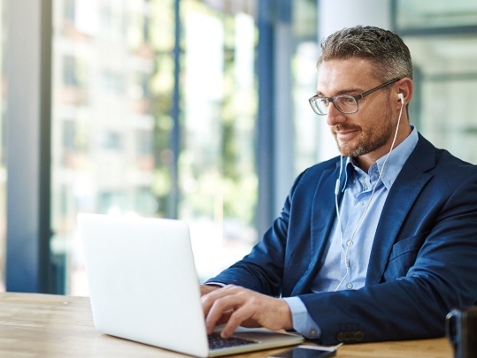 Businessman with glasses wearing earphones while using laptop at work.
