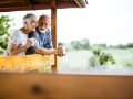 Mature smiling couple leaning on rail of porch ceramic coffee cups in hand.