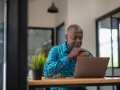 Man in casual clothes is focusing on a laptop screen, concentrating and thinking seriously.