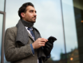Man wearing a coat and scarf with smartphone.
