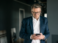 Man wearing jacket and glasses with smartphone.