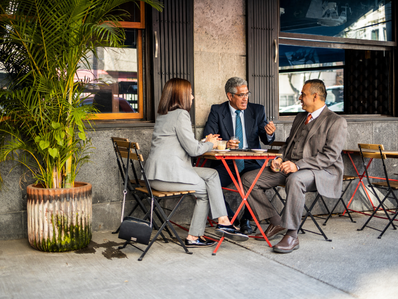 three older business people sitting at outdoor cafe and talking