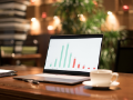 open laptop with vertical bargraph on screen, coffee in ceramic cup, on dark wood desk