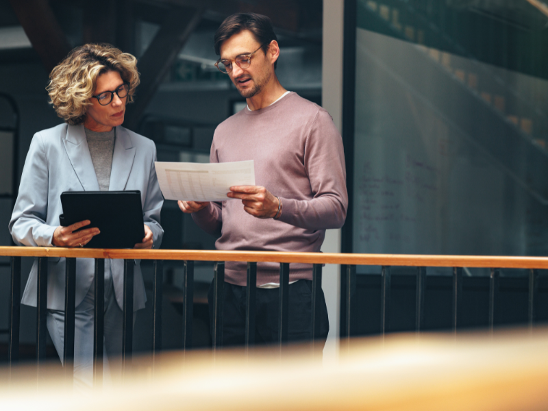 Business people standing near railing reading a document together.