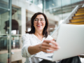 smiling young businesswoman sitting in office building, using laptop.
