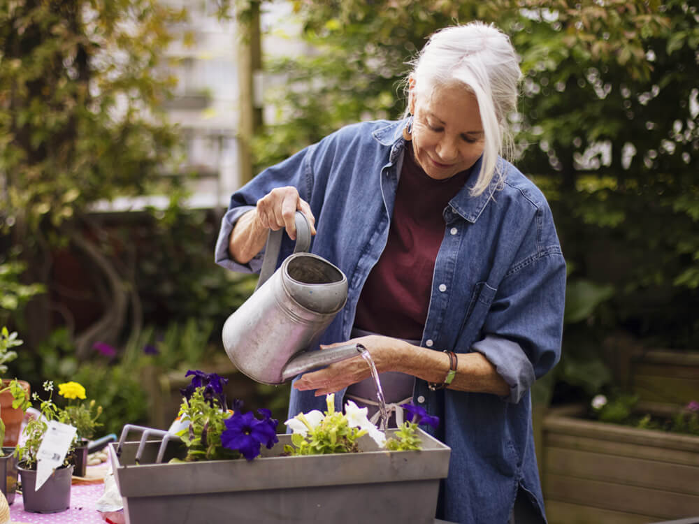 smiling older woman watering plants in plant nursery