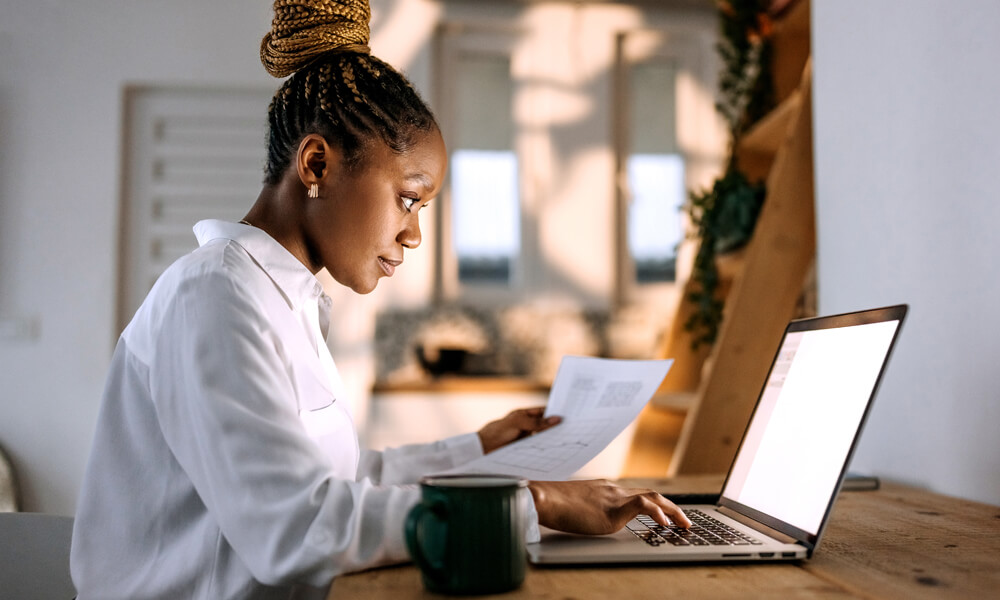 seated office employee comparing wealth management numbers from paper to laptop screen