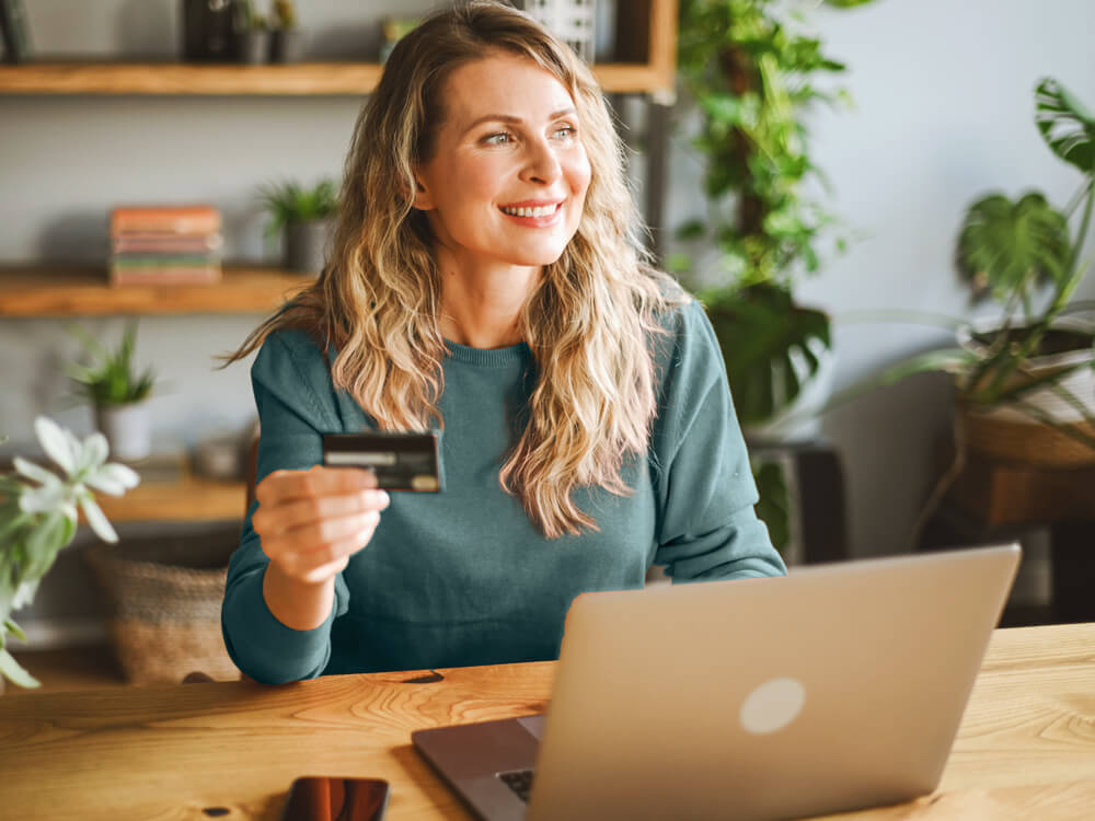 Financial advisor client smiling, credit card in hand, seated in front of laptop.