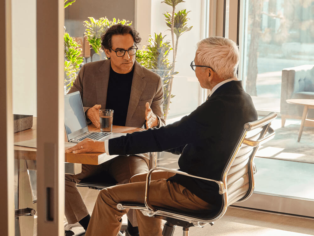 two seated business colleagues talking at desk with laptop