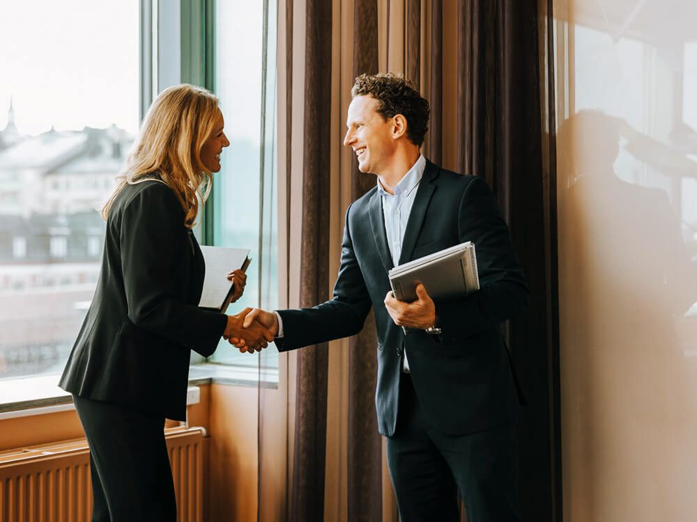 Businessman and businesswoman shaking hands in front of a window