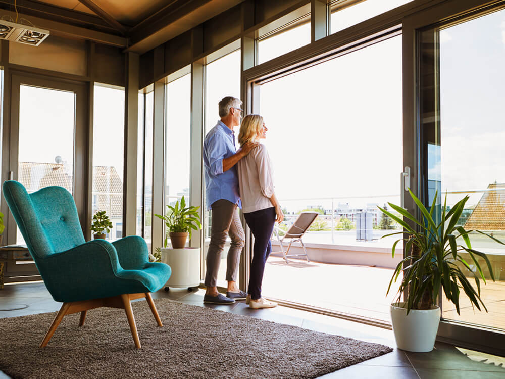 middle aged couple standing at open sliding glass door of home looking outside