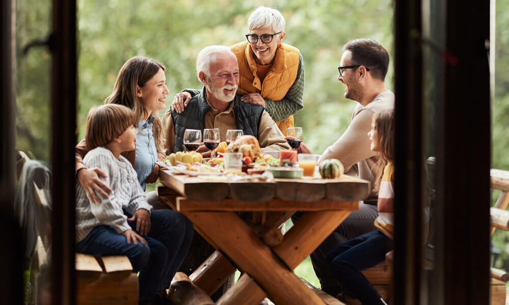 multi-generational family sitting outside at log picnic table, as seen through a big window