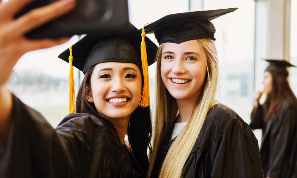 smiling college graduate women in cap and gown taking a picture