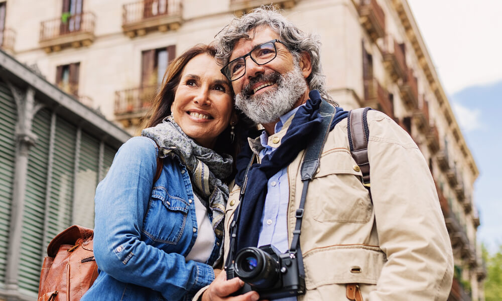smiling middle aged couple with camera outside in foreign city