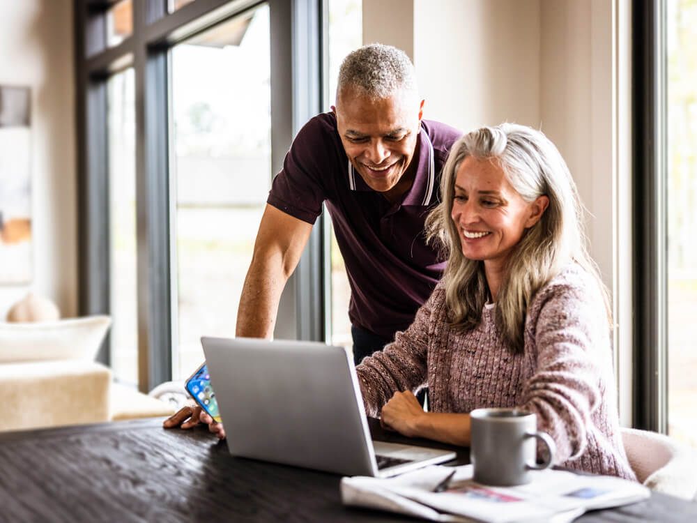 smiling middle aged couple looking at laptop searching for a financial advisor