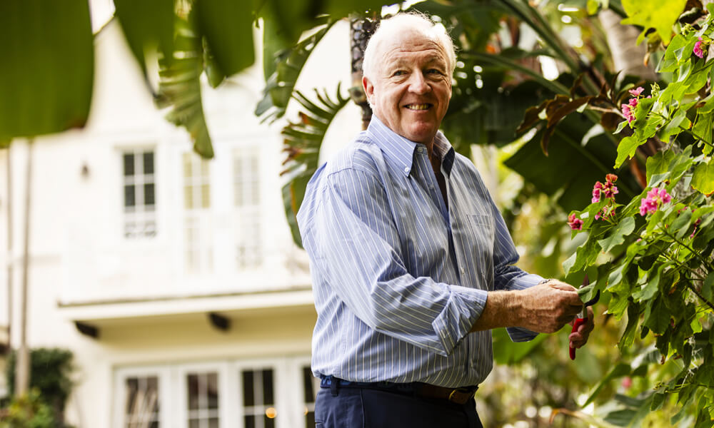 older man in relaxed business shirt outside touching leaves of flowery tree