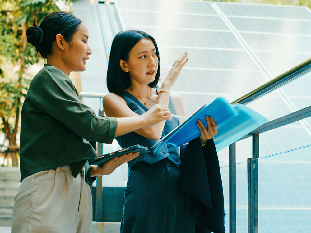 Two women reviewing paperwork and a tablet in an outdoor setting