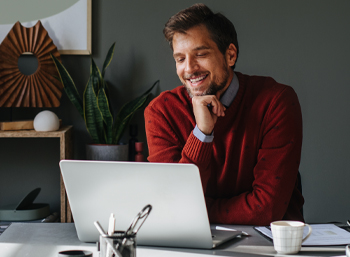 man in red sweater smiling at laptop