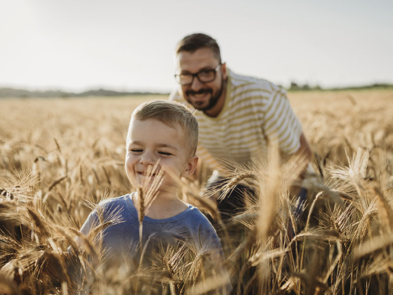 smiling father and son outdoors in a field of wheat