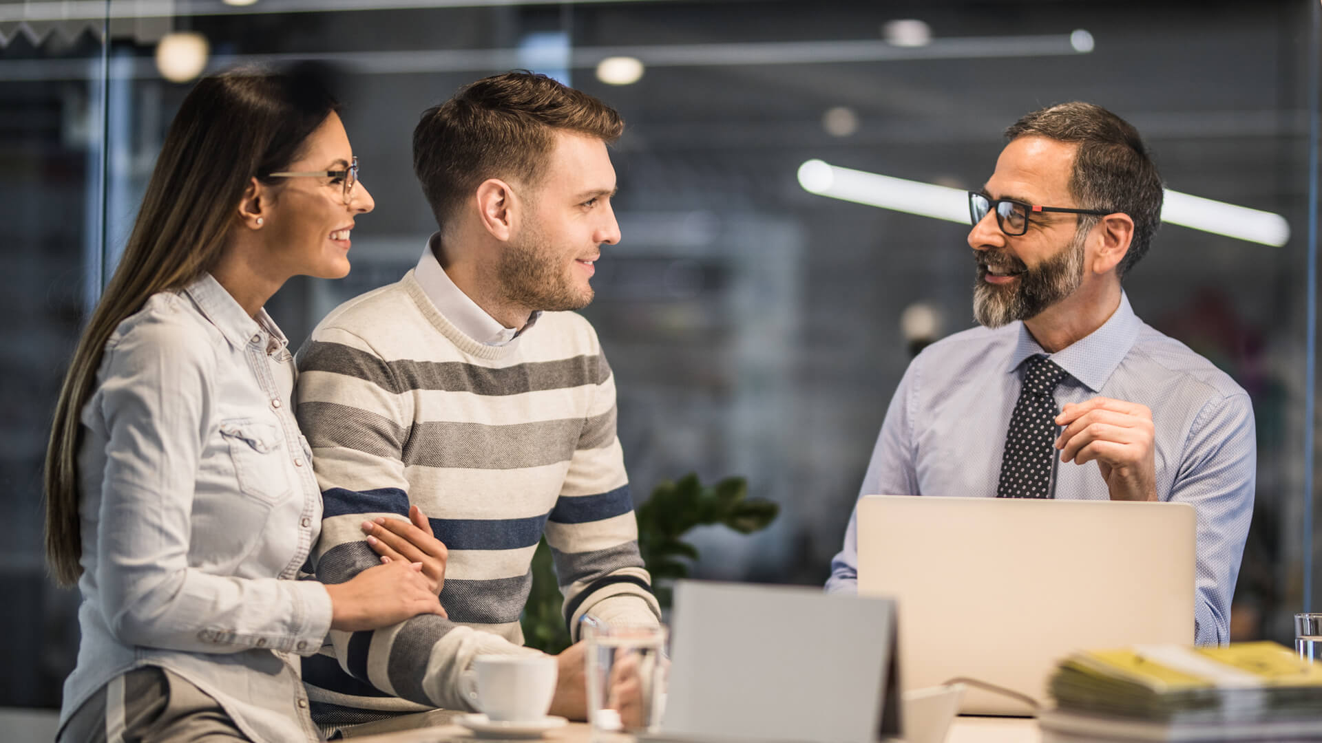 businessman with open laptop seated at table talking with couple
