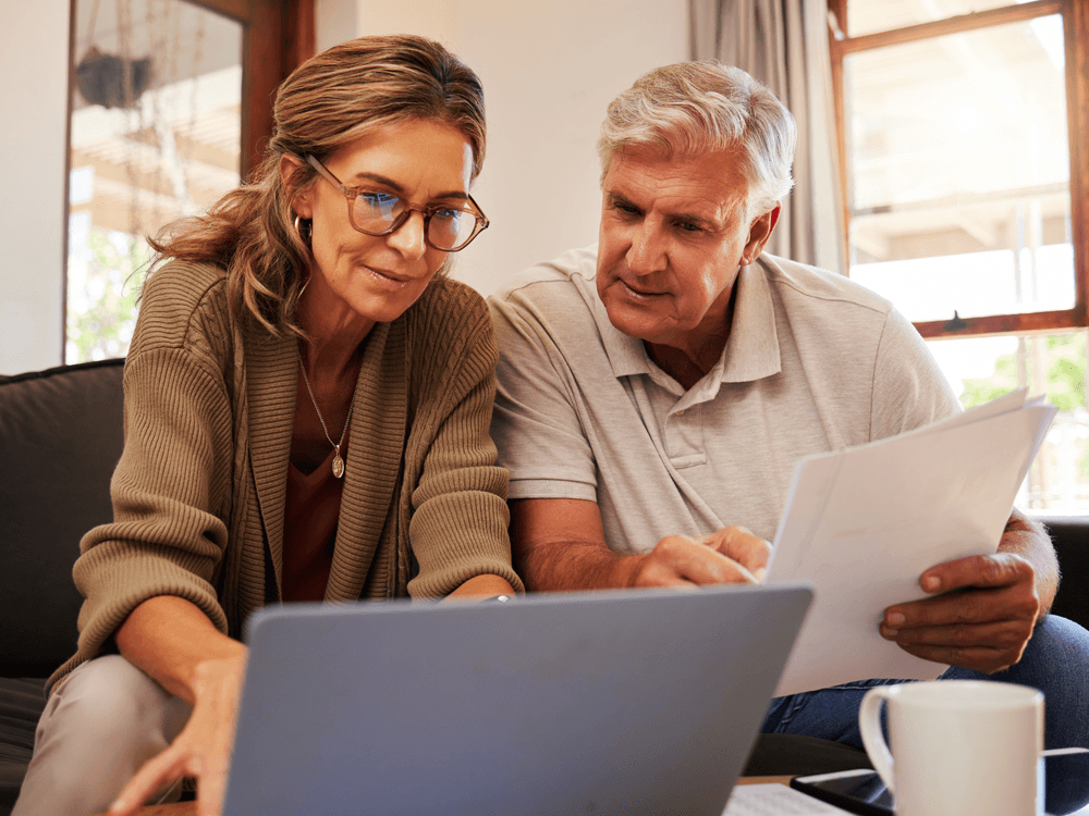 Smiling middle-aged couple sitting on sofa looking at their financial information.