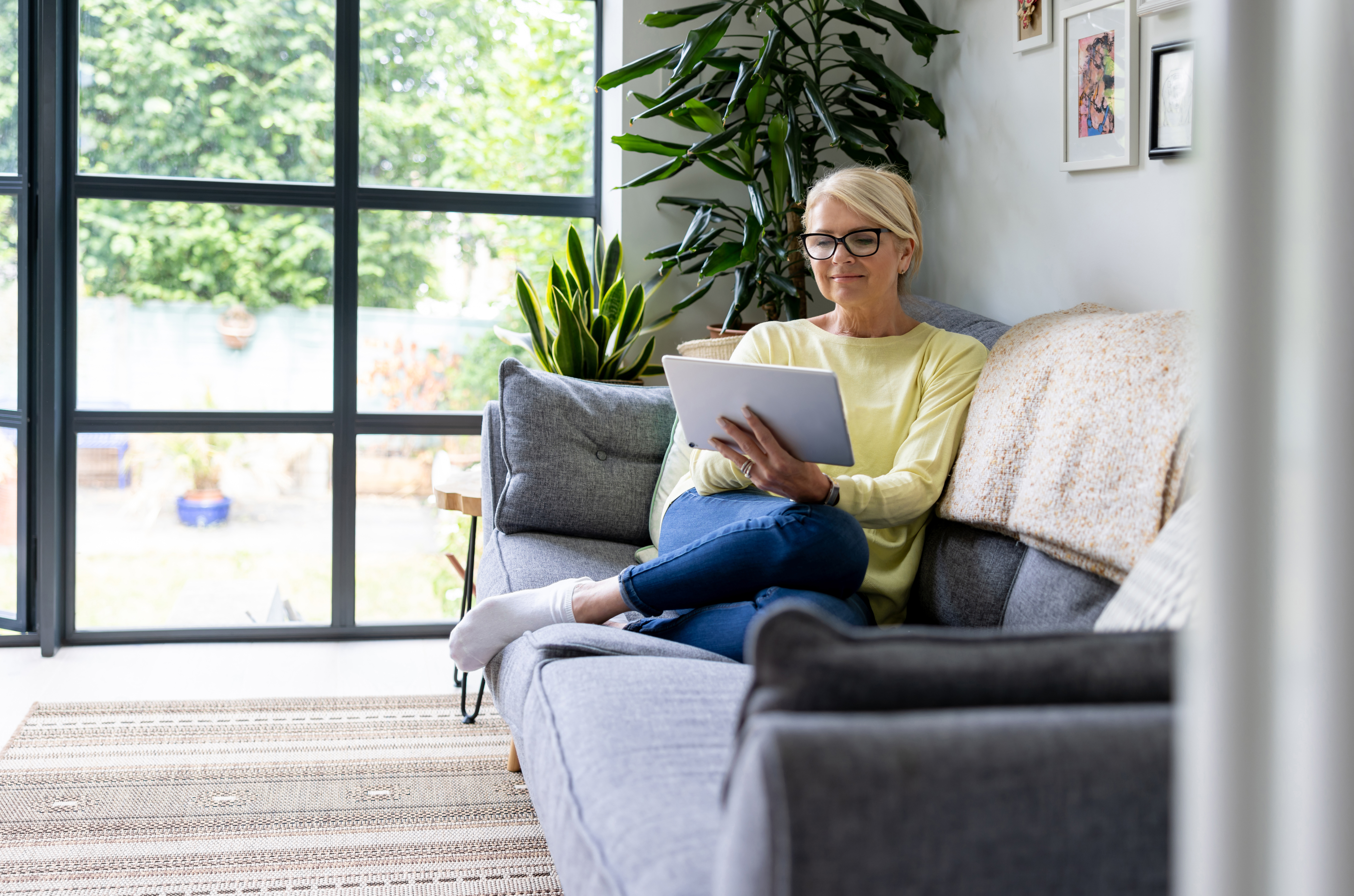woman at home sitting on couch looking at tablet in her hand