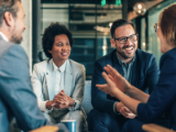 two business men and two business women seated at table talking