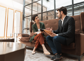 casually dressed, seated businessman and businesswoman talk